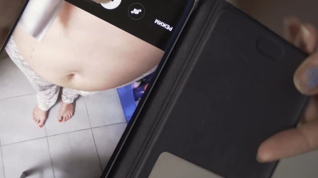 Close-up shot of pregnant woman taking mobile photo of her belly