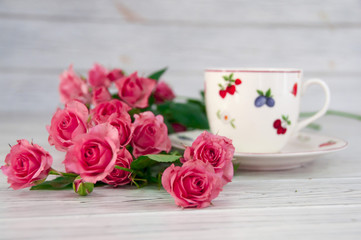 A cup of coffee on a saucer and small pink roses on a wooden table
