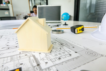 A wooden house model places on architect blueprint plan, laptop and engineering tools background in engineering room. Selective focus.