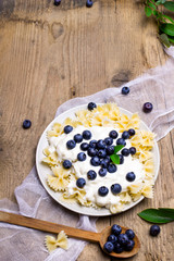 Tasty pasta with fresh organic blueberries and vanilla cream. Sweet dinner on retro wooden table.