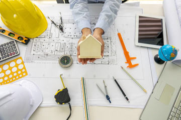 Engineering woman holding  wooden house model with architecture blueprint and equipment tools...