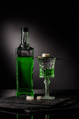 close-up shot of glass and bottle of absinthe with spoon and sugar cubes on dark background