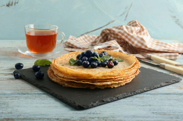 Slate plate with tasty pancakes and berries on wooden table