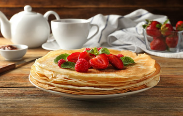 Plate with tasty pancakes and berries on wooden table