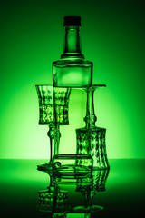 bottle of absinthe with lead glasses on reflective surface and dark green background