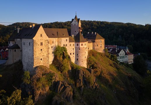 Aerial view on Loket Castle, Burg Elbogen, 12th-century Gothic style castle on a big rock, massive fortification illuminated by setting sun. Tourist place close to Karlovy vary, Czech republic.