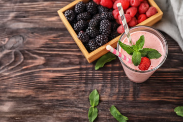 Glass with tasty raspberry smoothie and berries on wooden table