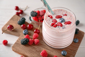 Glass with tasty raspberry smoothie and berries on light table