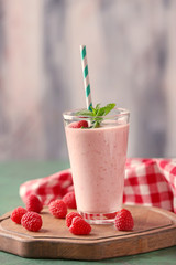 Glass with tasty raspberry smoothie on table against light background