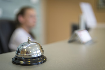 a silver bell of a hotel to meet guests against a blurry receptionist. an important accessory at...