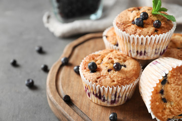 Wooden board with tasty blueberry muffins on table