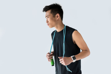 young asian sportsman with smartwatch holding jump rope isolated on grey background