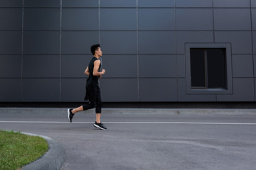 Fototapeta na wymiar side view of young asian sportsman in earphones running at city street