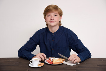 Portrait of a cute eating teenager on a white background at the table.