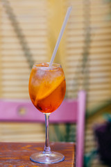 Aperitif cocktail consisting of prosecco, Aperol and soda water, stands in wine glass on wooden table in bar. Aperol spiritz cocktail with several cubes of ice and slice of orange.