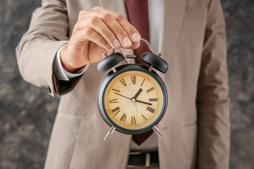 Businessman holding alarm clock on grey background, closeup. Time management concept