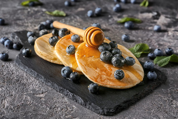 Slate board with delicious pancakes, honey and berries on grunge table