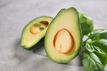 Tasty cut ripe avocados with basil leaves on grey textured background