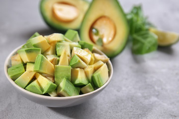 Bowl with cut avocado on grey table