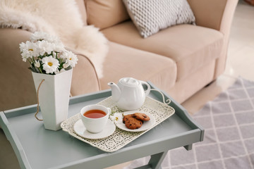 Obraz na płótnie Canvas Table with teapot and chamomile flowers in interior of living room