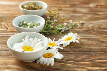 Fototapeta na wymiar Beautiful chamomile flowers with bowls on wooden background