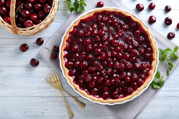 Tasty homemade pie and basket with ripe cherries on white wooden table