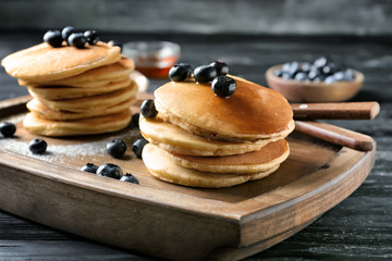 Board with delicious pancakes and berries on wooden table
