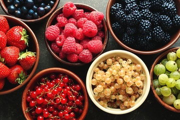 Bowls with various ripe berries on grey background, top view