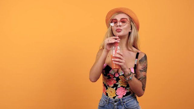 Hot sexy tanned woman enjoying a tropical dring while wearing a hat on yellow background. Copyspace available for your text, promotion or advertisement