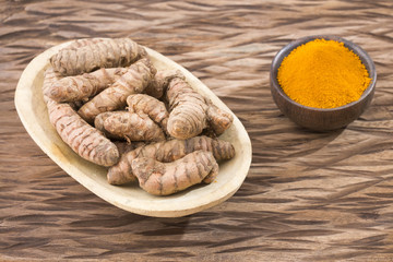 Turmeric powder and fresh turmeric on wooden background
