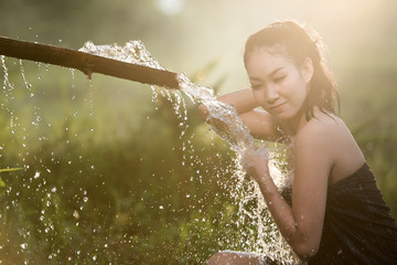 Asian girl taking a bath, the water flow with nature bamboo pipe