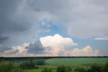 Beautiful scenic landscape in Ukraine in inclement weather - forests, fields of sunflowers and meadows. Breaks through the clouds the blue sky.