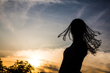 Silhouette of braided hair teenage girl turning around / Urban sunset scene. Millennial Generation