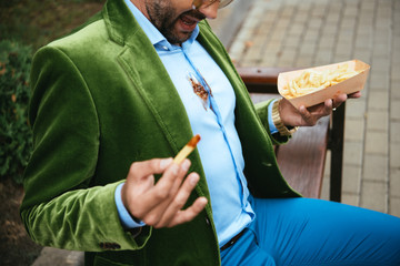 partial view of man in green velvet jacket with ketchup on shirt and french fries in hands sitting...
