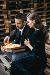 side view of stylish couple with italian cheese pizza resting on street