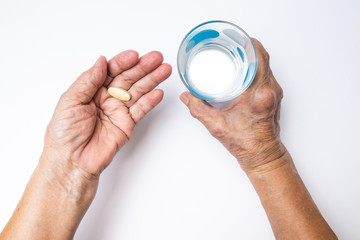 Senior woman's hands holding Vitamin C pill with polka dot glass of water, Healthcare and medical concept