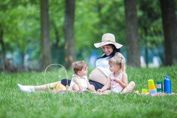 Young pregnant mother with two girls on a picnic playing