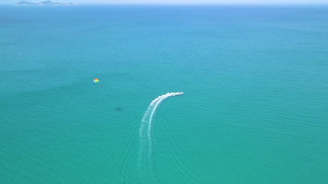 Colorful parasail flying over blue sea pulled boat aerial view. Parasailing over blue sea drone view. Summer activity and extreme entertainment while resting on resort beach.