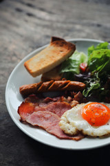 English breakfast  fried egg, ham,sausage, bacon,salad and toast on wood background in mystic light