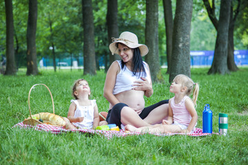 Young pregnant mother with two girls on a picnic playing