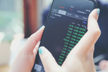 Close up on woman hand holding smartphone trading stock and data in coffee shop background business concept