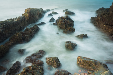 Long exposure seascape with foamy waves splashing against a rocky shore of thailand in the morning...