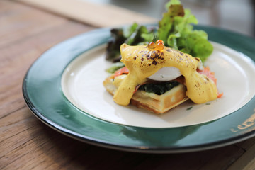 Breakfast food egg benedict , poached egg with yellow sauce with waffle and smoked salmon on wood background