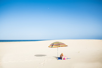 wonderful endless beach desert for the best relax during holiday summer time. lady lay down and take the sun. umbrella and hat colored. shadow on the white sand. ocean in background. enjoy 