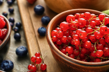 Bowl with red currant on wooden board