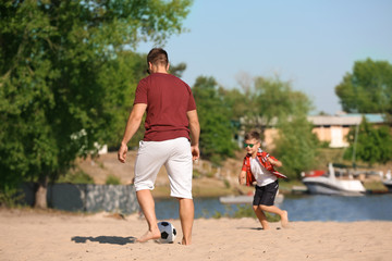 Little boy with his dad playing football on sand beach