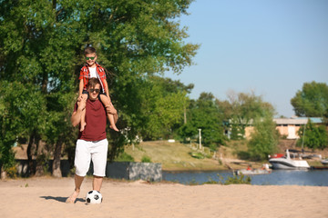 Little boy and his dad with soccer ball on sand beach