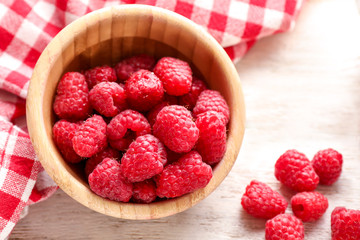 Wooden bowl with sweet ripe raspberries on table