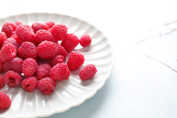 Plate with sweet ripe raspberries on table