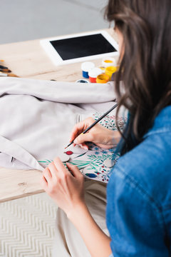 female fashion designer painting on jacket at working table in clothing design studio